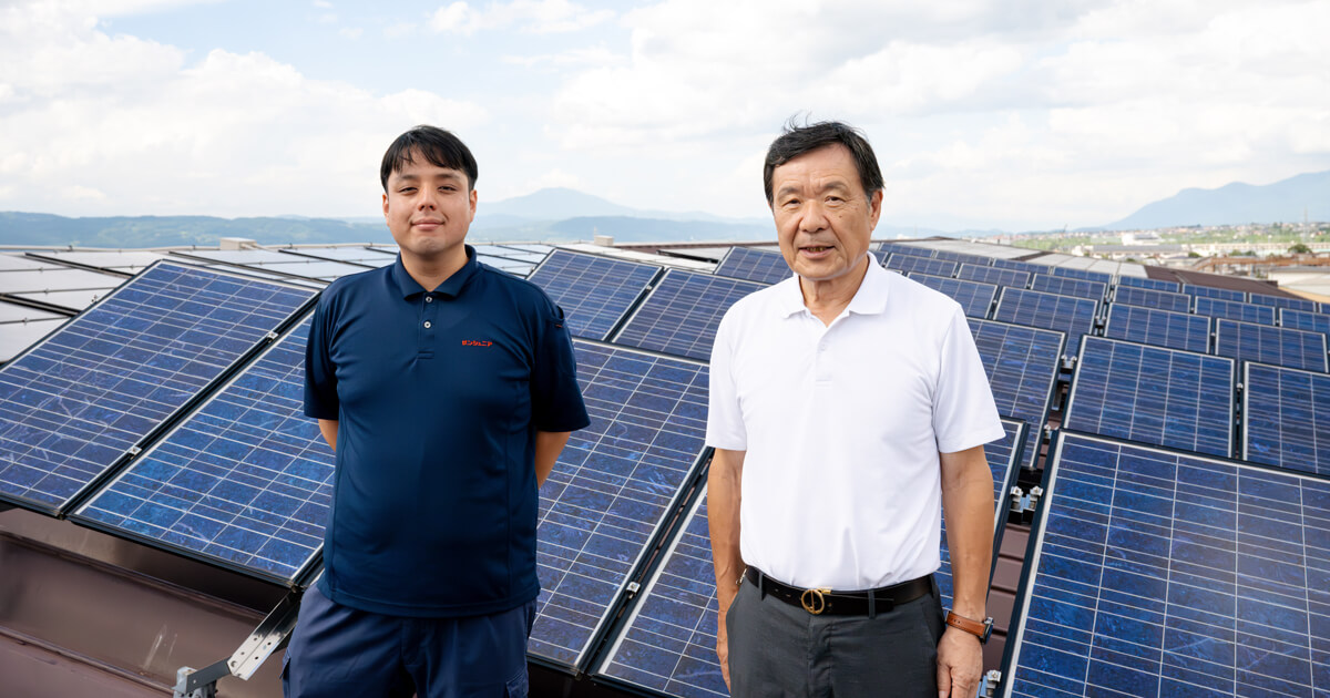 本社屋根に設置した太陽光パネルの前に立つ青木様（左）、西原様（右）