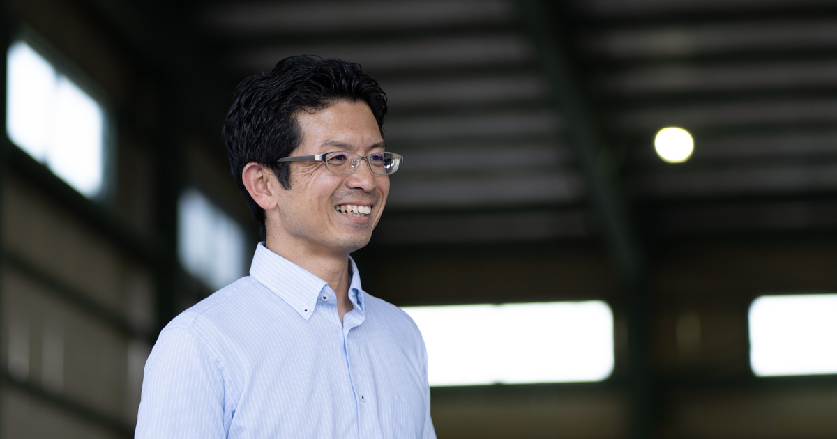 自社倉庫の前で笑顔を見せる髙木様
