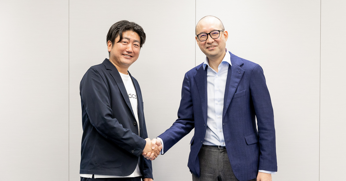 カメラに向かって握手をする山崎（左）、末吉様（右）